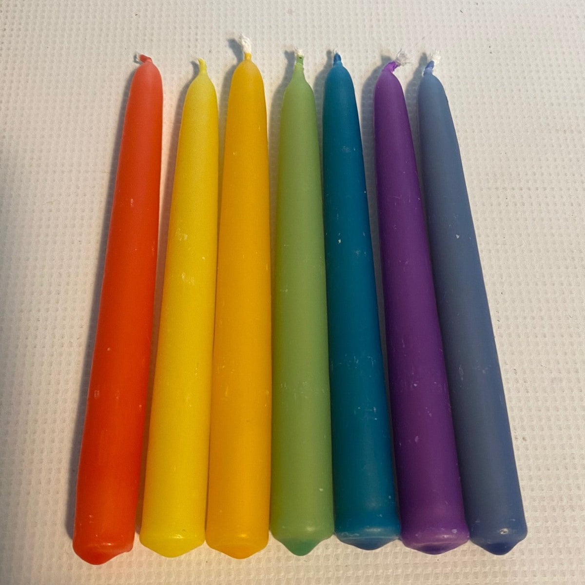 Seven colorful taper candles in a rainbow sequence of orange, yellow, green, blue, and purple
